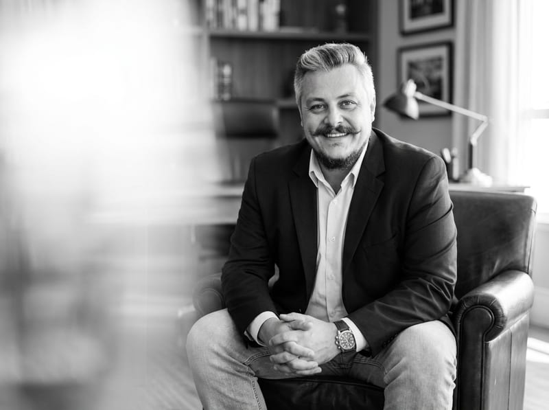 Vinicius Lanzi de Carvalho — Perito Avaliador Imobiliário, sentado em escritório com biblioteca ao fundo